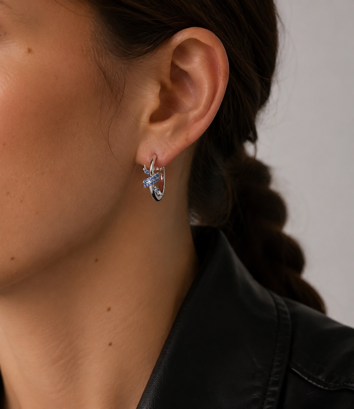 Close-up of a woman wearing elegant white gold-tone C-hoop earrings with micro-paved blue zirconia knots.