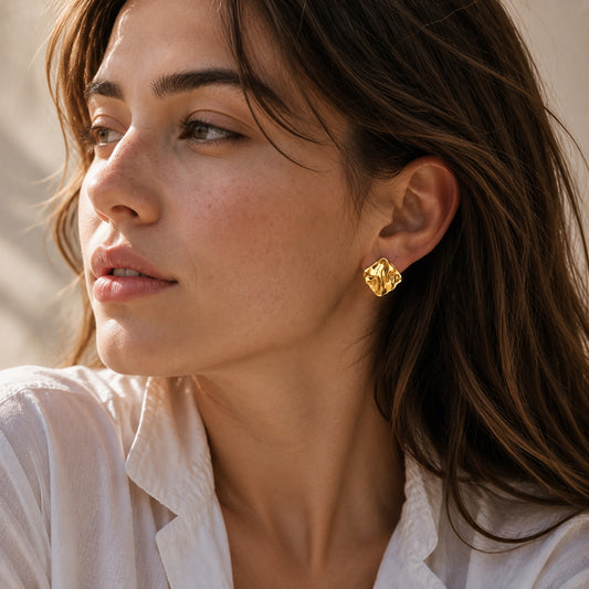 Beautiful woman wearing 18K gold-tone sculptural crinkled square stud earrings bathed in warm, natural sunlight.