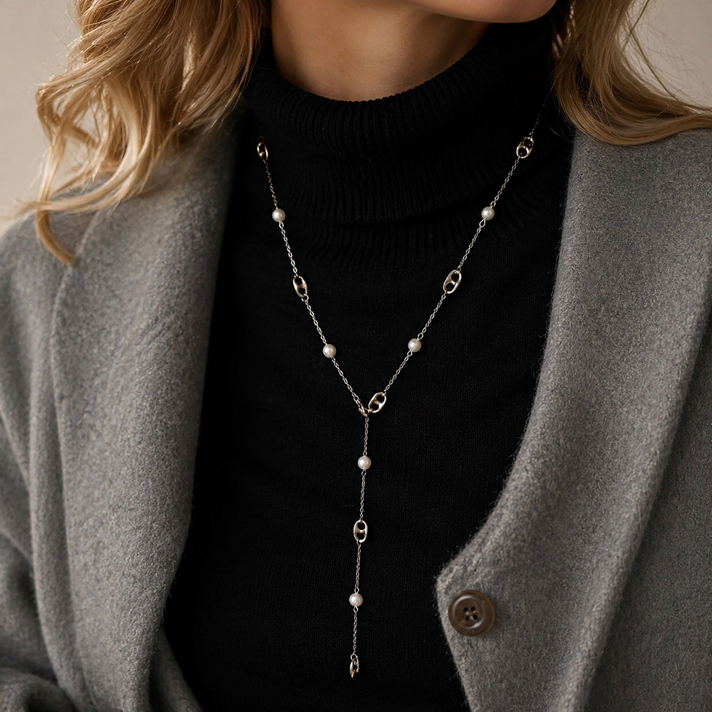 Woman styling a silver-tone pearl lariat necklace over a black turtleneck sweater.