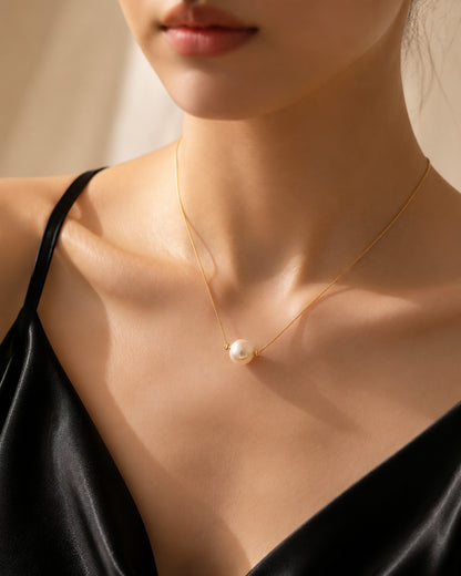 Woman wearing a minimalist single pearl gold-tone necklace with a black slip dress.