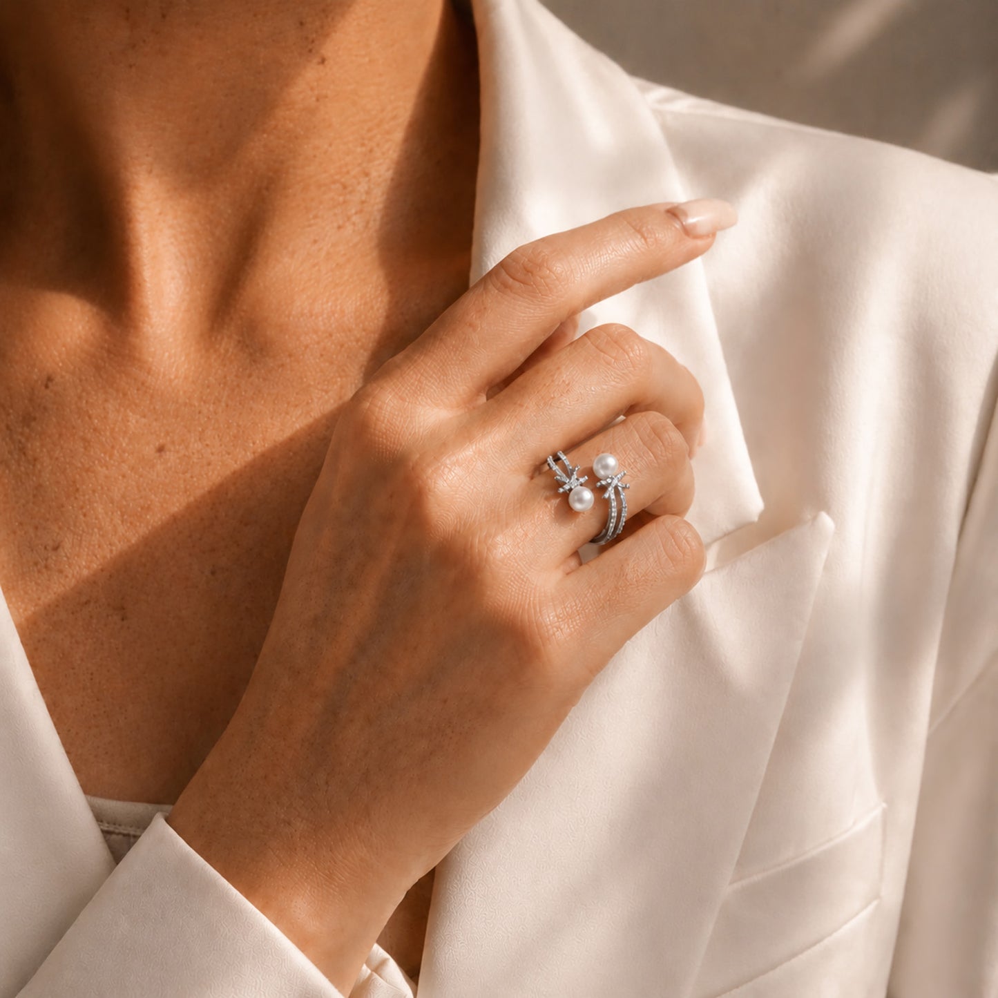 Elegant woman styling a white gold-tone open bypass ring featuring sparkling zircon knots and freshwater pearls against a classic white blazer.