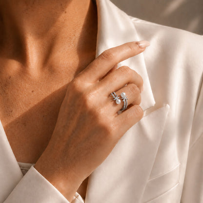 Elegant woman styling a white gold-tone open bypass ring featuring sparkling zircon knots and freshwater pearls against a classic white blazer.